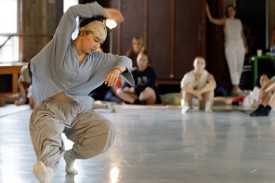 Person dancing in casual clothes in a open studio with people on sidelines